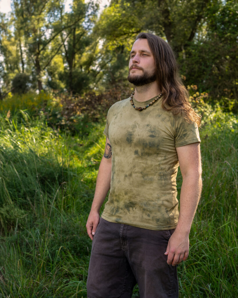 Grünes, körperbetontes T-shirt mit abstraktem Bleichemuster, getragen von einem langhaarigem Mann in der Natur.