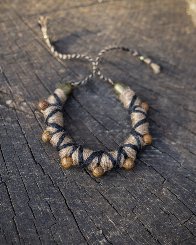 Beiges Armband mit eigearbeiteten Holzperlen und schwarzen Verzierungen, präsentiert auf rustikaler Holzoberfläche.